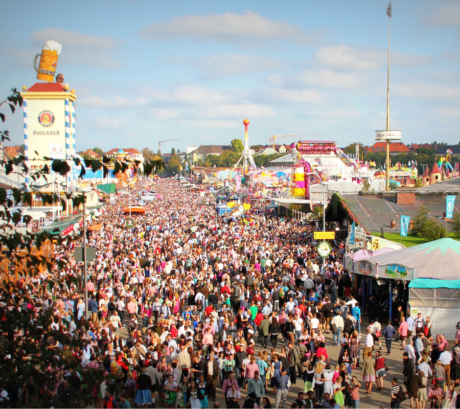 Vista panorámica del Oktoberfest con muchas personas disfrutando al aire libre, rodeadas de atracciones y puestos tradicionales
